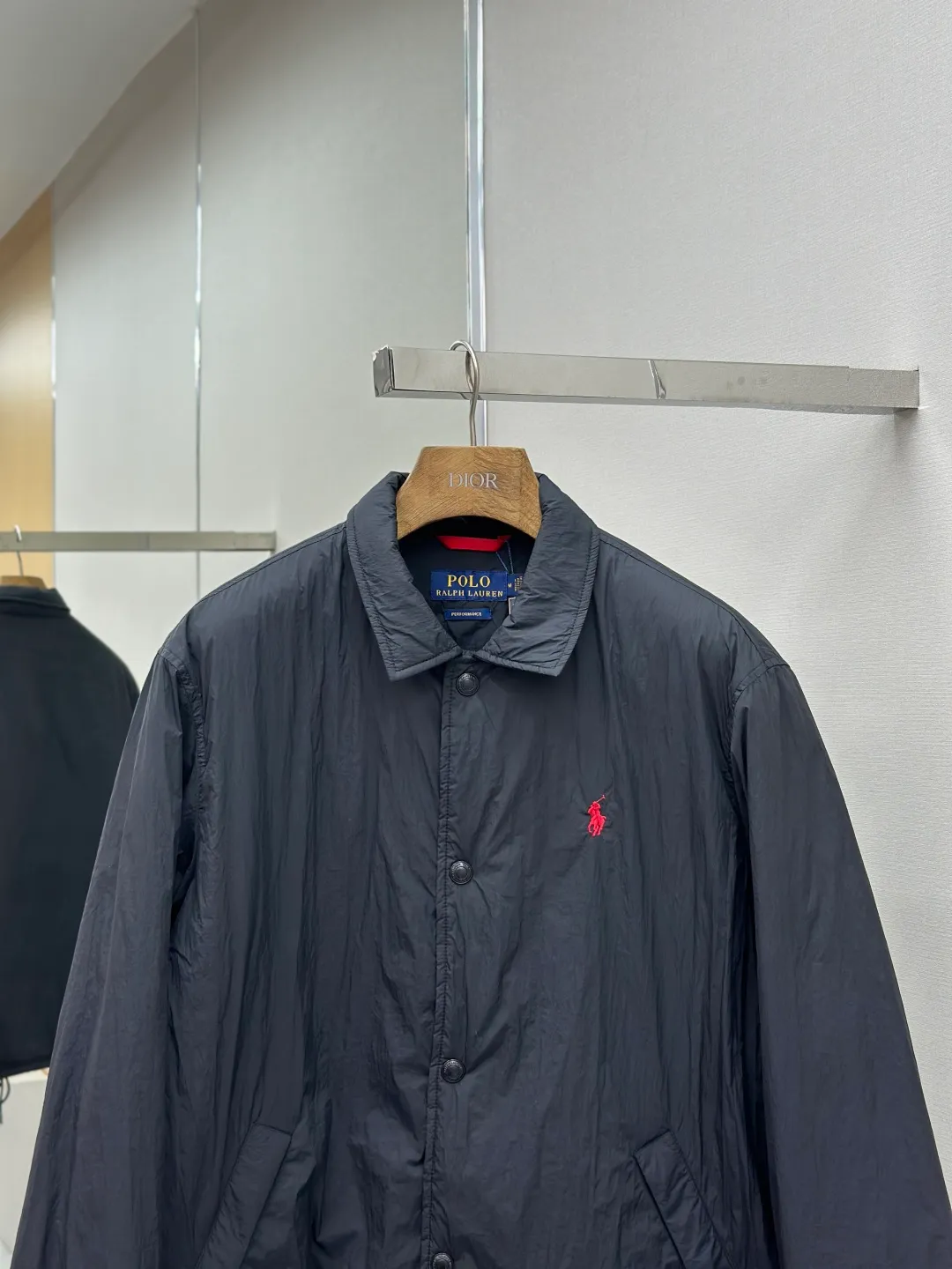 P650 RAH LAUREN RL red label lapel is light and thin. It is made of high-density nylon taffeta with a density of about 210T-300T. The surface is smooth and slightly matte. It has excellent windproof and waterproof performance (with R water-repellent treatment). It has strong wrinkle resistance and is easy to care for. It adopts the vat dyeing process (the dye penetrates into the fiber) and the color fastness reaches ISO level 4 or above to avoid fading or color transfer after washing. The lightweight cotton-polyester blend lining (65% Polyester + 35% Cotton) reduces the friction between the fabric and inner clothing and improves the smoothness of wearing. The blended material combines breathability and durability to avoid the stuffy feeling of pure nylon lining. The classic coach (Jaet) loose fit has a slightly dropped shoulder line (the shoulder width is 1-2cm wider than the standard fit), the length reaches the hips, and the sleeves are slightly tapered straight sleeves, taking into account freedom of movement and casual style. Flat satin stitch embroidery (satin embroidery), using 100% polyester high color fastness embroidery thread (the color number is consistent with the brand's standard red color card), the stitch density is 12-15 stitches cm, the outline of the horse logo is clear, and the details of the rider and horse are burr-free. Precise positioning through the template (12cm from the bottom of the collar and 8cm from the placket) ensures symmetry and centering. The seams of the body are made of double-needle flat seams (needle pitch 3cm, 10 needles), the stitches are flat and straight, the stitching color is dark black (the same color as the fabric), and the stitch width is 0.5cm, which enhances firmness and forms simple decorative lines. The placket is made of double-layer folding + flat seam splicing, with a thickness of about 0.3cm to ensure that the buttons are not easily deformed when fixed; the edges of the placket are cut with a hot knife to avoid burrs. The armholes are machine stitched with round head keyholes and flat seams. After stitching, the armholes have a natural curvature and no sense of tightness during movement. The height of the sleeves is about 8-10cm, which is in line with the casual and loose characteristics. Black urea resin button with matte surface treatment. The buttonholes are hand-made keyholes (6 strands of cotton thread, keyhole density of 8 stitches mm), and the edges of the eyelets are smooth and without burrs. The first button on the neckline is a hidden button (diameter 12mm), which prevents the neckline from opening and improves the neatness of wearing. Size:S-XL